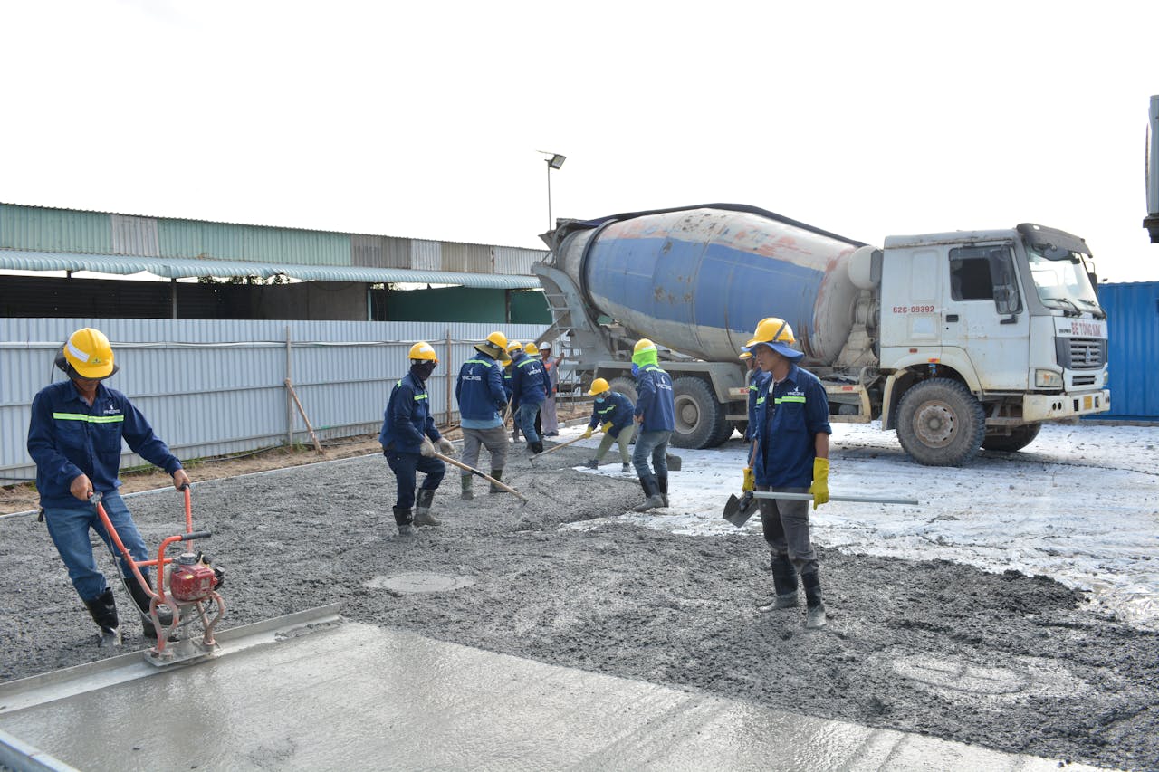 Workers in safety gear pouring concrete outdoors with a cement mixer truck.
